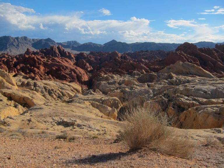 desert lanscape consisting of brown gravel in the foreground yellow rocky landscape behind it then chocolate cliffs behind that and grey mountains in the background