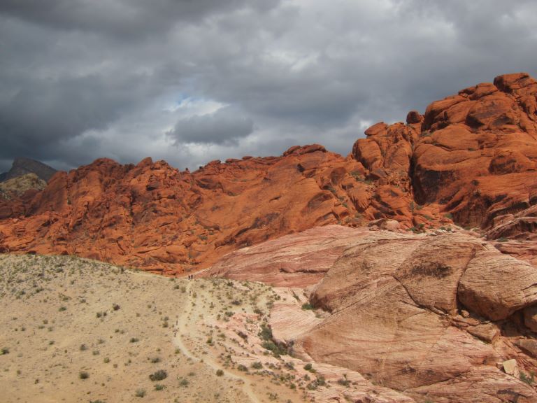 bright red and pink canyon walls against a gray cloudy sky and brown ground